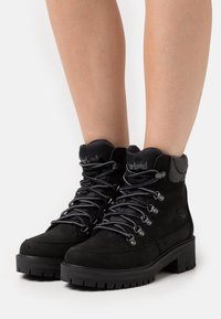 Scarpe da trekking nere in suede con occhielli metallici, lacci grigi e una suola spessa con battistrada; altezza alla caviglia con colletto imbottito per il comfort.