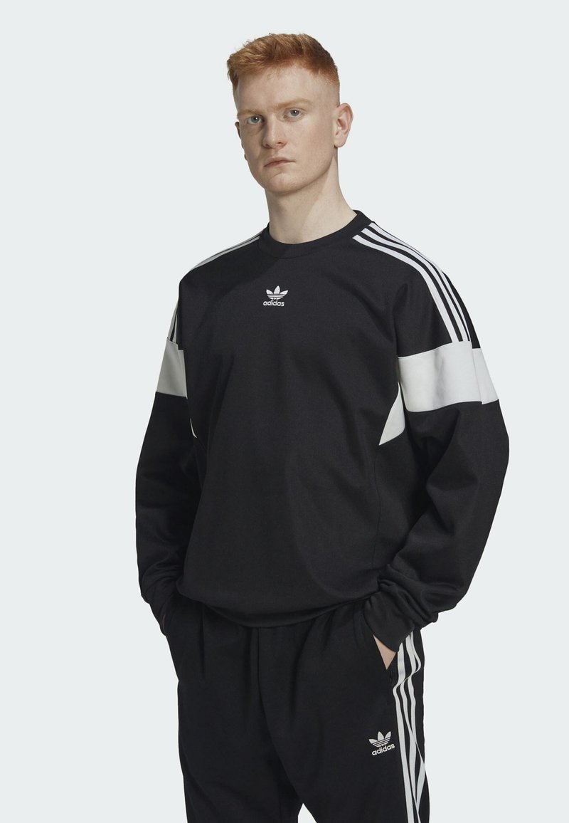 Musta urheiluhuppari, jossa on valkoiset korostuspaneelit ja kolme valkoista raitaa hartioilla. Hupparissa on pyöreä kaula-aukko ja logo rinnassa.