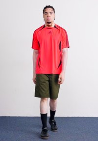 Red athletic shirt with black accents, paired with olive green shorts. Black socks and shoes complete the outfit. Simple design and breathable fabric.