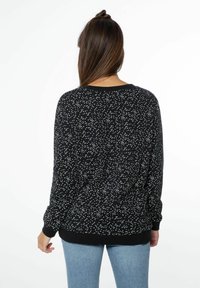 Maglione nero con motivo a pois bianchi, scollo rotondo, maniche lunghe, polsini e orlo a costine. Il tessuto sembra morbido con una vestibilità comoda.