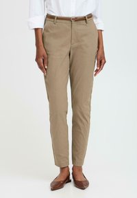 Beige kalhoty na míru se slim střih, s hnědým pásem, bočními kapsami a nažehlenými sklady vpředu. Hnědé ploché boty.