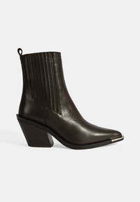 Bottine en cuir noir avec un pointu, des détails de couture verticales et un talon épais. Elle dispose d'une languette pour un enfilage facile.