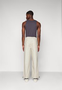 Top sin mangas de color gris oscuro y pantalones beige con cintura elástica. Los pantalones son livianos, tienen un corte recto y lazos en el dobladillo.
