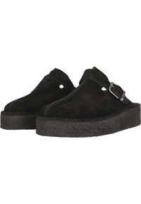 Svarta mocka slip-on skor med en strukturerad skumkloss och justerbar metallspänne. Funktioner öppna sidor och en rundad tådesign.