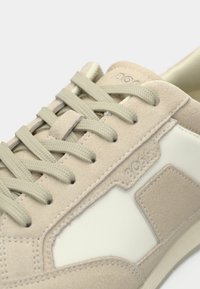 Baskets en daim beige et crème avec lacets assortis, coutures détaillées et nom de la marque embossé sur le panneau latéral.