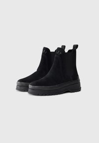 Schwarze Wildleder-Ankelstiefel mit elastischen Seiteneinsätzen und einer robusten schwarzen Gummisohle mit einem strukturierten Profil für besseren Halt.