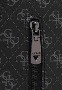 Borsa nera con zip realizzata in tessuto testurizzato che presenta un motivo ripetuto di logo. Il tirazip ha una finitura metallica e un marchio inciso.