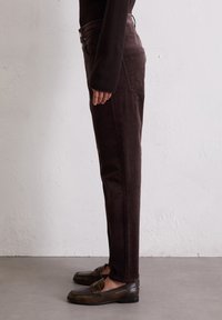 Bruine corduroy broek met een slim fit, voorzien van een hoge taille, pocketdetails en een soepele textuur. Gepaard met donkerbruine instappers.