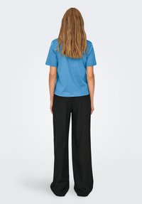 Maglietta di cotone blu con maniche corte, abbinata a pantaloni neri a gamba larga. L'outfit presenta una vestibilità comoda e una texture liscia.