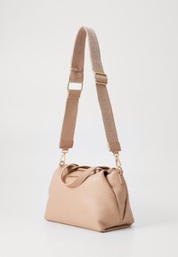 Bolsa de couro em tom areia clara, com superfície texturizada, alças duplas no topo e uma alça de lona destacável com o nome da marca em bege. Detalhes em metal dourado.