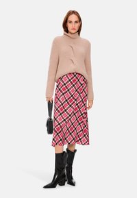 Beige gerippter Strickpullover mit hohem Kragen, kombiniert mit einem pinken und schwarzen gemusterten Midirock und schwarzen Lederstiefeln über das Knie.