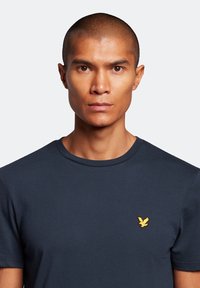 Maglietta di cotone blu navy a maniche corte con scollatura a girocollo, caratterizzata da un piccolo logo di un'aquila gialla sul lato sinistro del petto.