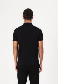 Svart pikétröja med korta ärmar, mjuk textur och klassisk krage. Har en figurnära design och rakt fåll längst ner.