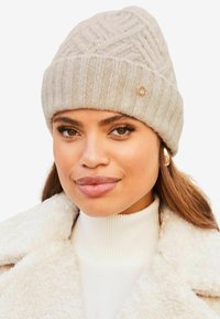 Lys grå strikket beanie med ribbet bånd og geometrisk mønster, med en lille gul accent. Materialet ser blødt og struktureret ud.