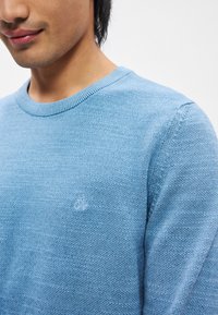 Ανοιχτό μπλε πλεκτό πουλόβερ με ριγωτό στρογγυλό λαιμό και μικρό κεντημένο λογότυπο στο στήθος. Μαλακή υφή και �άνετη εφαρμογή.