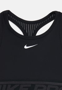 Svart treningstopp med dyp utringning, med hvit Nike-logo på brystet og teksturert stripete design bak.