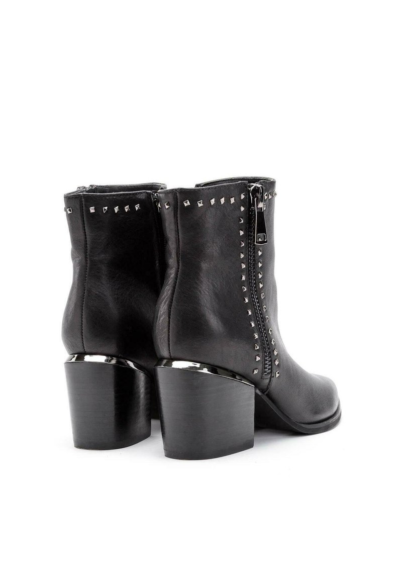 Botas de tobillo de cuero negro con cierre de cremallera, con tachuelas metálicas a lo largo de los lados y un tacón negro grueso.