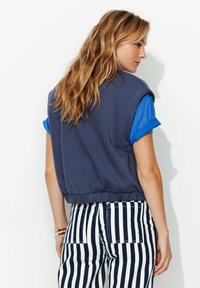 Sweatshirt court bleu marine à manches roulées bleues, associé à un pantalon rayé taille haute. Dispose d'une taille élastique et d'une coupe décontractée.