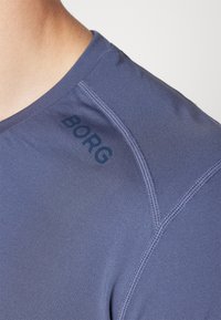 Kratke športne majice iz modrega blaga, z okroglo ovratnikom, ravnimi šivi in napisom "BORG" na rami. Gladka tekstura.