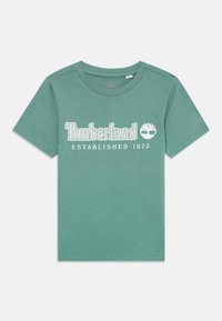 Grønn bomull t-skjorte med korte ermer, med teksten "Timberland" og "Etablert 1973" i hvit tekst, rund hals, glatt tekstur.