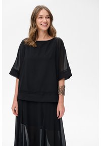 Czarny top warstwowy z luźnymi, przezroczystymi rękawami i solidnym korpusem. Posiada dekoracyjne przeszycia na dole. W zestawie ze spódnicą w tym samym kolorze.