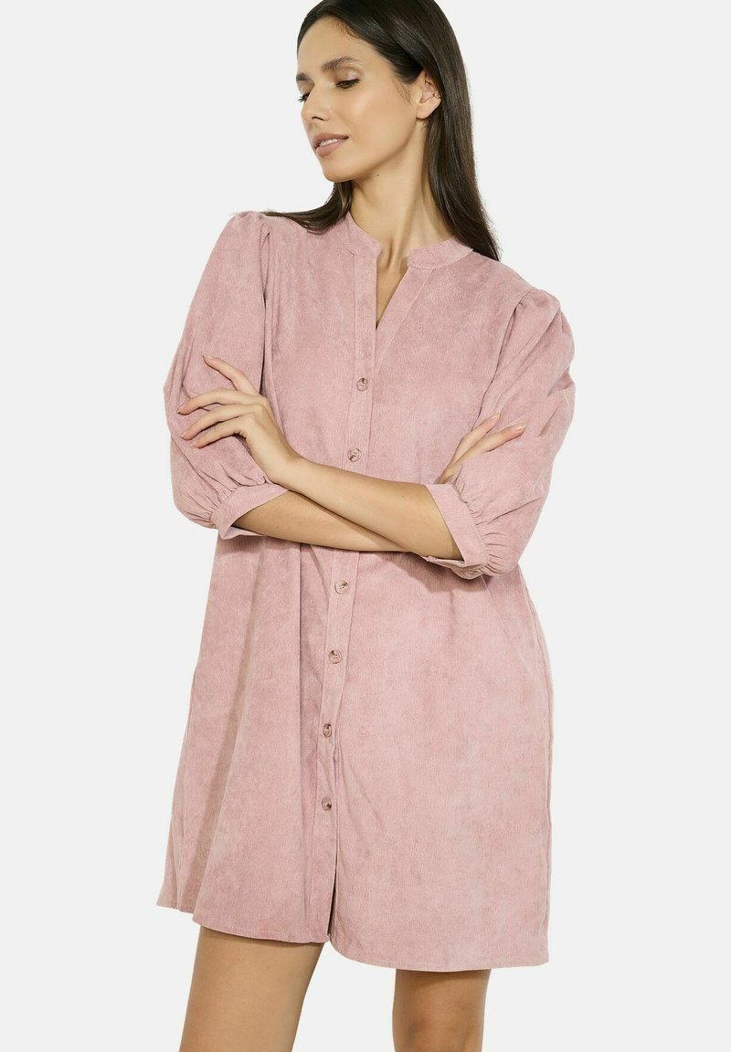Abito button-up rosa pallido con colletto, maniche a sbuffo corte e una texture morbida. Presenta una forma dritta e un design fino al ginocchio.