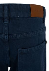 Pantaloni in denim blu scuro con una toppa in pelle etichettata "TRUSSARDI" in vita, con una tasca sul lato destro e cuciture standard.
