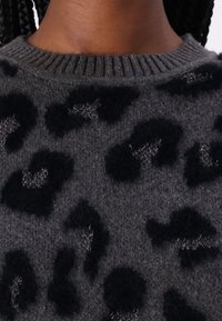 Maglione lavorato a maglia grigio scuro con stampa leopardata nera, caratterizzato da un collo rotondo a coste e un tessuto morbido e testurizzato. Piccole accentuazioni metalliche visibili.