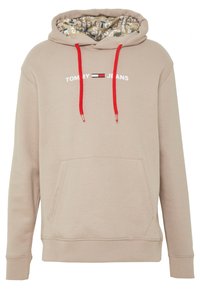 Sudadera con capucha beige con bolsillo frontal, cordones rojos y texto blanco "TOMMY JEANS". La capucha forrada tiene un interior con patrón. Textura suave.