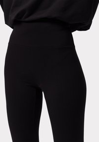 Černé legíny vyrobené z měkkého, elastického materiálu s vysokým pasem. Design je přiléhavý, s hladkým povrchem a bez viditelných vzorů.