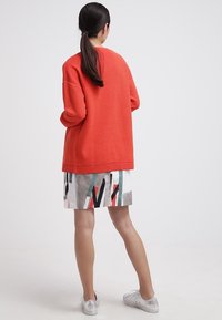 Röd ribbad tröja som matchas med en mönstrad kjol med geometriska former i grått, svart och grönt. Inkluderar silverskor.