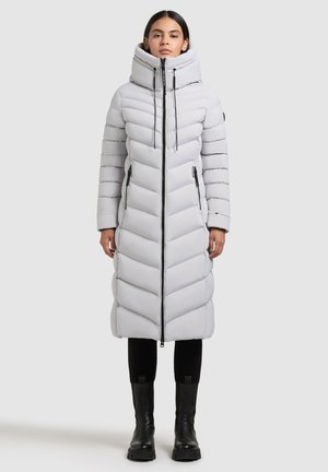 Lunga giacca a vento bianca con colletto alto, trapuntatura a zig zag, zip frontale e tasche laterali. Abbinata a stivali neri alti e leggings.