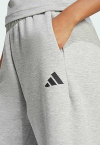 Szare sportowe dresy wykonane z miękkiej mieszanki bawełny, z elastycznym pasem, bocznymi kieszeniami oraz czarnym akcentem logo na udzie.
