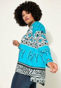 Blauw shirt met een patroon van abstracte designs, inclusief dierenprints en tekst, met wijde mouwen en een gebogen zoom.