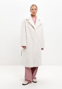 Vitt fuskpälsjacka med bred krage, långa ärmar och en avslappnad passform, som har en slät textur och subtila sömdetaljer.