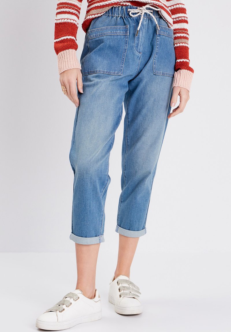 Pantalons jogger en denim bleu clair avec une taille à cordon, ourlets resserrés et deux poches arrière. Associés à des baskets blanches avec des accents métalliques.