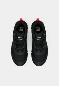 Pantofii sport negri au un exterior texturat, cusături albastre contrastante și o banderolă roșie la călcâi. Șireturile sunt negre cu accente argintii.