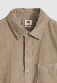 Πουκάμισο με κουμπιά σε μπεζ βελούδινο ύφασμα, με κλασικό γιακά, τσέπη στο μπροστινό μέρος και δύο κουμπιά, με  υφή υφάσματος και χαλαρή εφαρμογή.