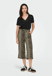 T-shirt noir avec encolure en dentelle, pantalon large à motifs léopard, et baskets noires à semelles en caoutchouc, avec une coupe décontractée et des poches avant.