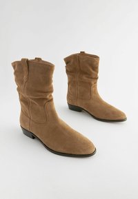 Bottes chevilles en daim marron avec un design décontracté, des orteils pointus et de petits talons blocs. Dispose de panneaux latéraux sans couture et de languettes pour un enfilage facile.