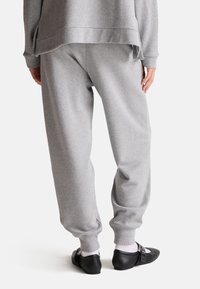 Szare bawełniane dresy o luźnym kroju, z ściągaczami na końcach nogawek i miękką fakturą, połączone z czarnymi płaskimi butami i białymi skarpetkami do kostek.