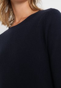 Granatowy sweter wykonany z miękkiego materiału, z okrągłym dekoltem i klasycznym krojem. Faktura wydaje się gładka i lekka.