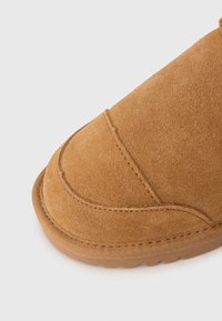 Brune ruskind ankelstøvle med rund tå, der har syninger og en tekstureret sål. Blødt materiale og minimalistisk design.