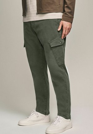 Grüne Cargo-Hosen mit Seitentaschen, geradem Schnitt, aus Baumwollmaterial mit feiner Textur, kombiniert mit weißen Sneakers.