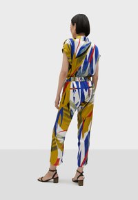 Tuta multicolore con vita aderente, maniche corte e un vivace motivo a foglie in blu, giallo, rosso e bianco.