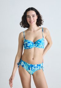 Mėlyna ir akvamarinė bikini maudymosi kostiumėlis su prigludusia, raštuota viršutine dalimi ir šoninėmis raišteliais. Lygi tekstūra, reguliuojamos petnešėlės ir įvairūs abstraktūs mėlyni raštai.
