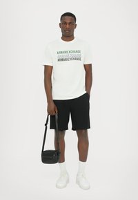 Balsama t-krekls ar daudzkrāsainu "Armani Exchange" grafiku, apvienots ar melniem šortiem un baltām kedām. Nēsā nelielu melnu crossbody somiņu.