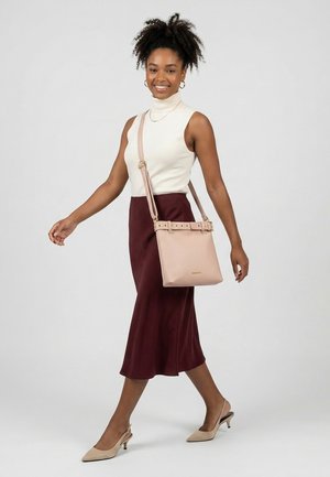 Kvinde med krøllet hår iført en hvid ærmeløs top, mørkerød nederdel, beige hæle og bærer en lyserød skuldertaske.
