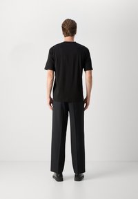T-shirt noir à manches courtes en tissu lisse, associé à un pantalon large noir. La vue de dos met en avant la simplicité et le design minimaliste.