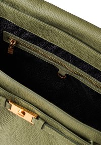 Interieur einer grünen Lederhandtasche, das eine Reißverschlusstasche mit goldenen Beschlägen zeigt. Das Material ist strukturiert und hat ein dunkles gemustertes Futter.